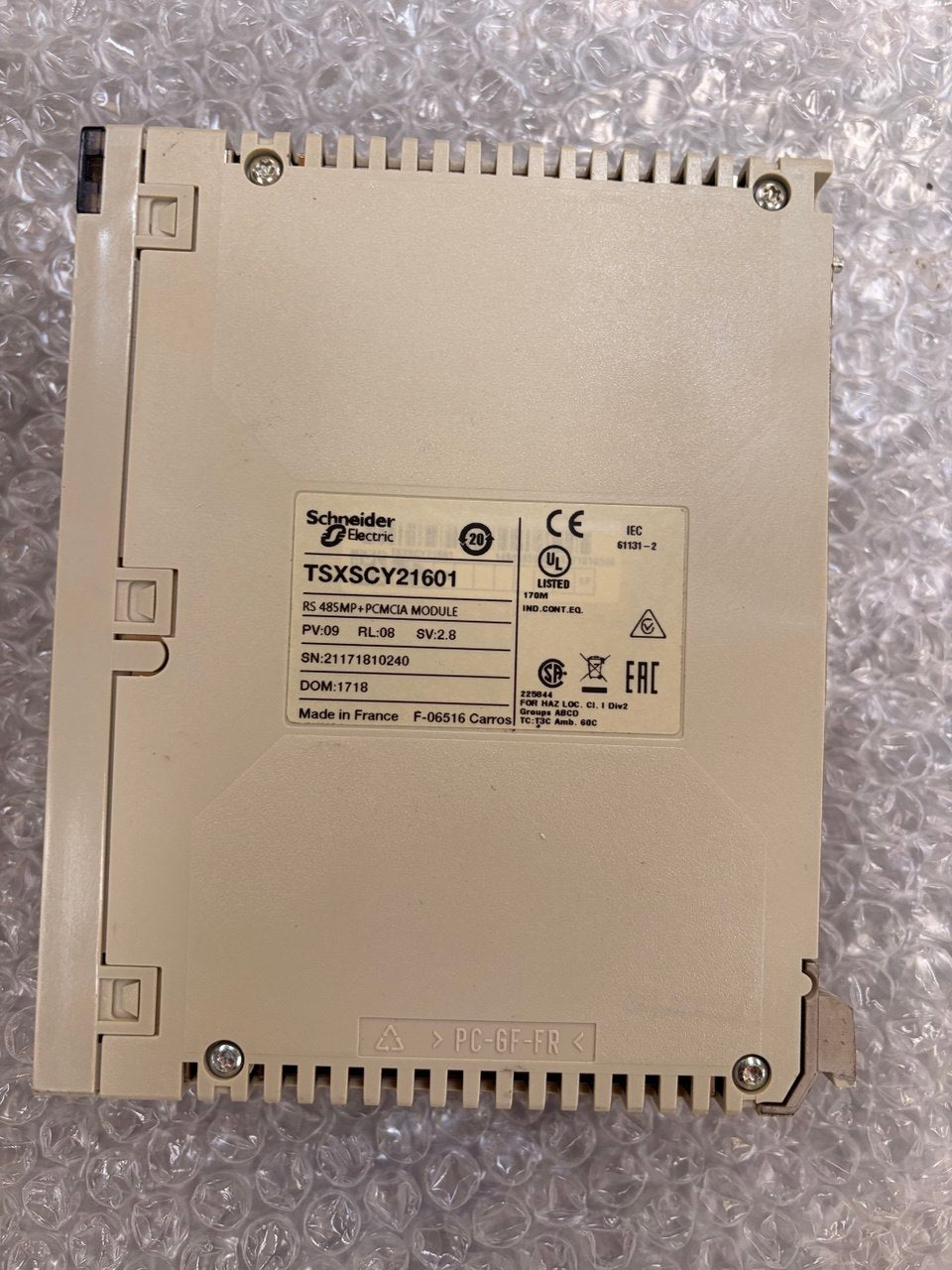 Schneider Electric TSXSCY21601 industrial control module in beige plastic, showing the back with screw terminals and a central label with regulatory markings, placed on bubble wrap.