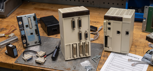 A workbench displaying various Schneider Electric Modicon Quantum and Premium PLC spare parts, cables, and an inventory checklist.