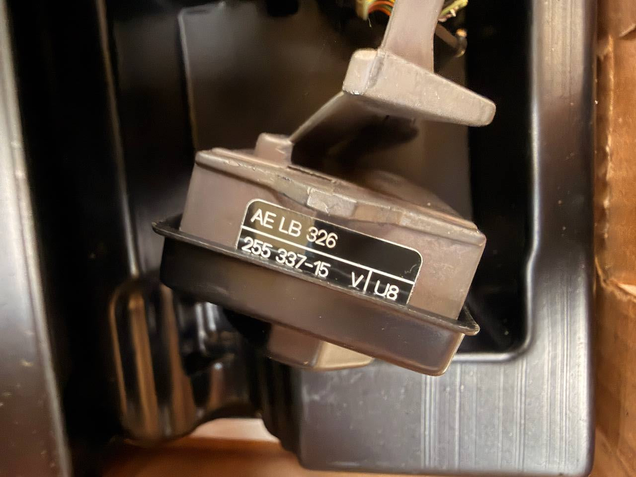 A close-up of a black plastic electrical switch component with printed white text reading 'AE LB 326' and voltage/phase markings, resting inside a dark compartment.