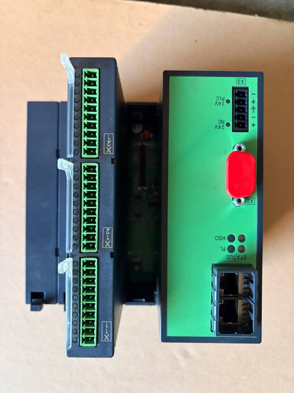 Heidenhain electronic modules, one green with a red button and the other black with green connectors, on a beige surface.