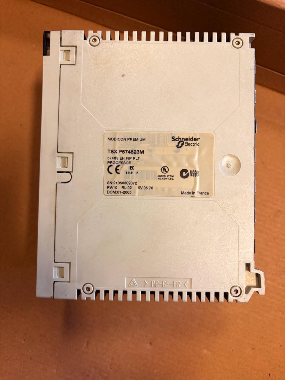 Schneider Electric industrial electronic module TBX PS174625M on a brown cardboard background.