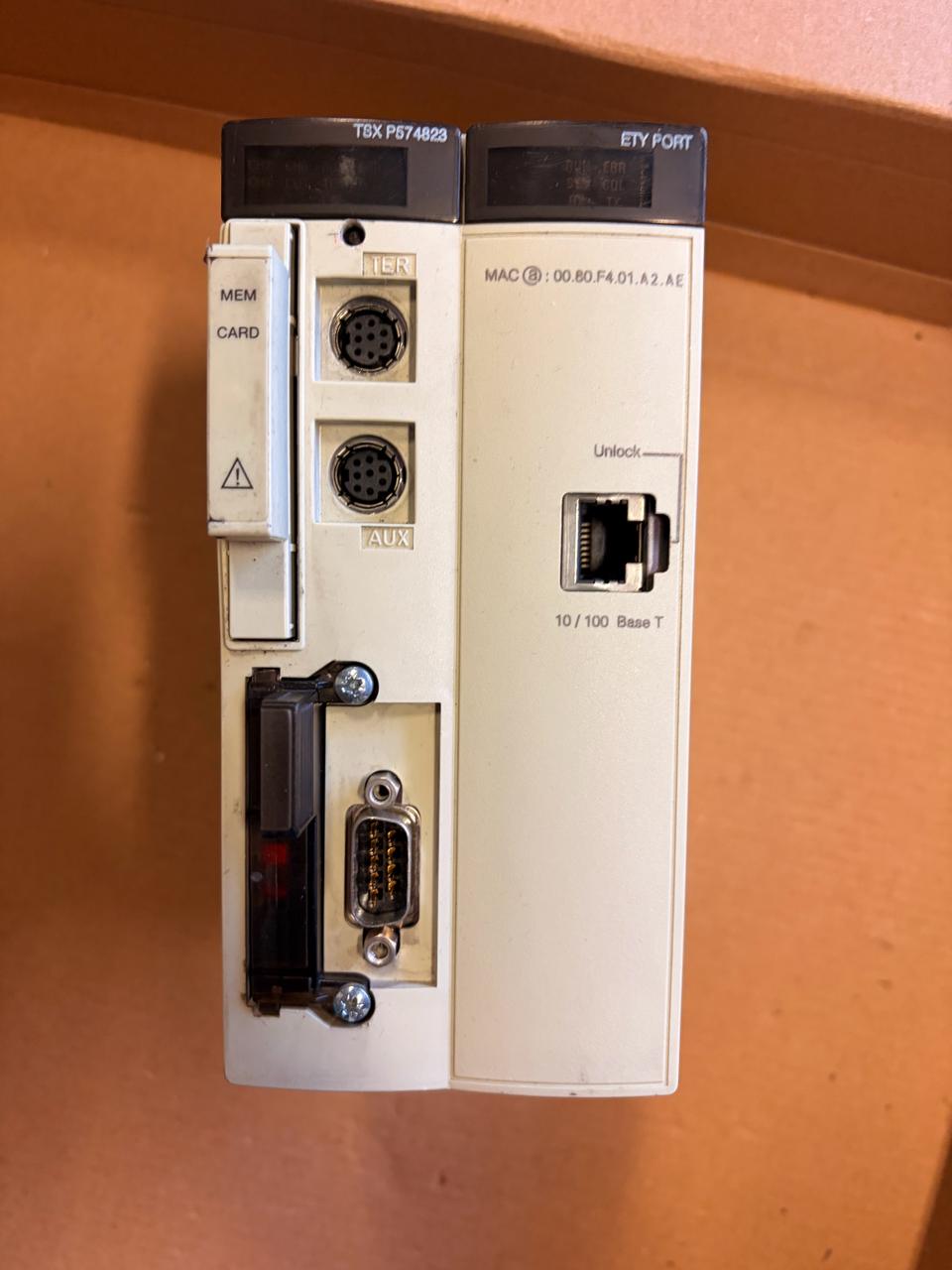 A Schneider industrial PLC module, specifically the TXP 620/620-2 variant, with its front panel removed to show the rear ports and connectors, resting on a brown cardboard surface.