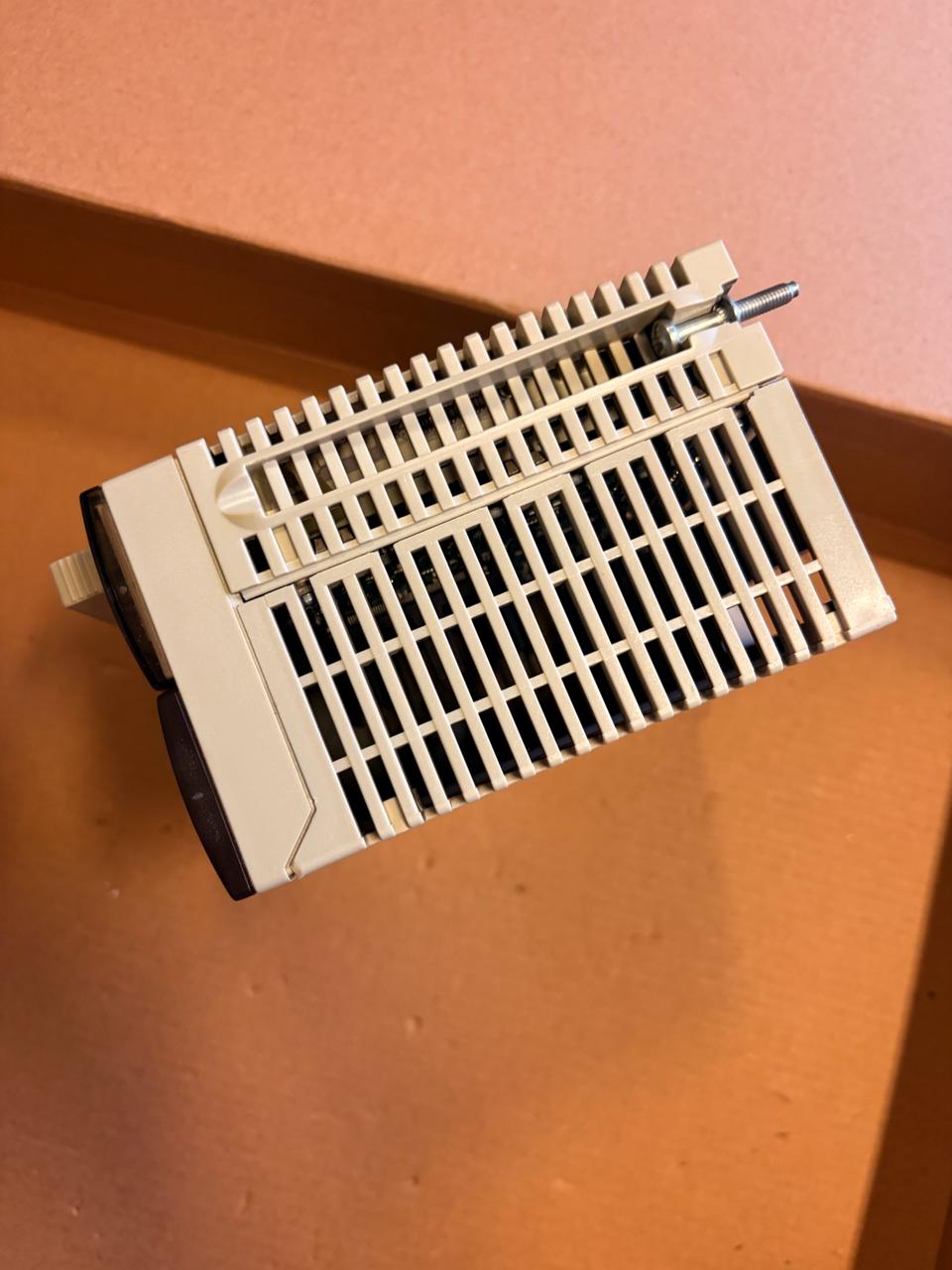A beige plastic replacement filter or grille with a slotted front and a metal pin attached, resting on a brown cardboard surface.
