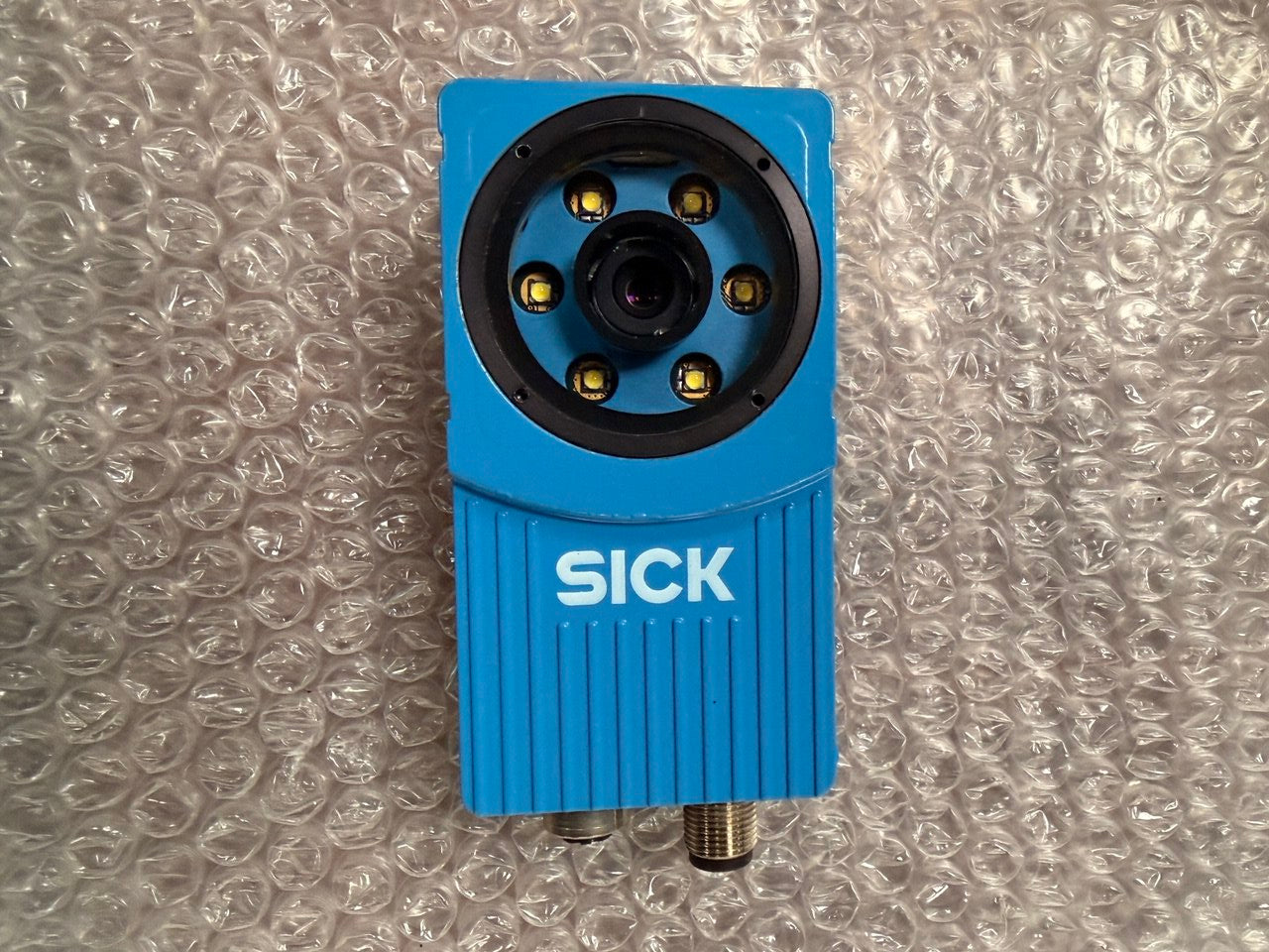 Blue sensor with 'SICK' branding on a bubble wrap background