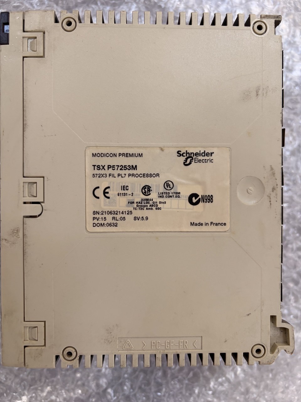 Schneider Electric TSX PF725S3M industrial electronic module with a beige plastic housing and a central white label, photographed from above on a textured gray surface.