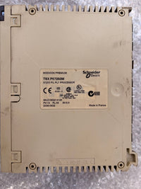 Schneider Electric TSX PF725S3M industrial electronic module with a beige plastic housing and a central white label, photographed from above on a textured gray surface.