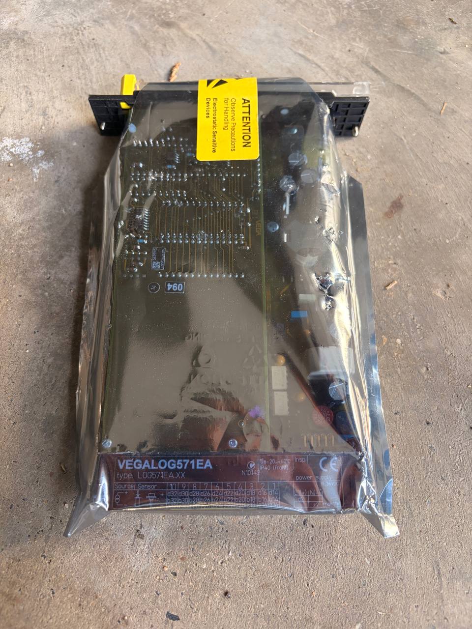 Vegalog Electronic component in clear packaging with a yellow label on a concrete surface